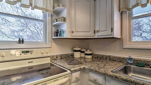 Una cocina con estufa, horno, encimera de granito, pileta de acero inoxidable y armarios blancos.