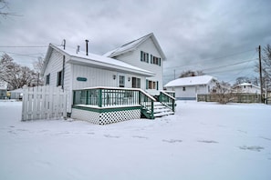 Ein weißes, zweistöckiges Haus mit einer grünen Veranda und Treppen, umgeben von Schnee.