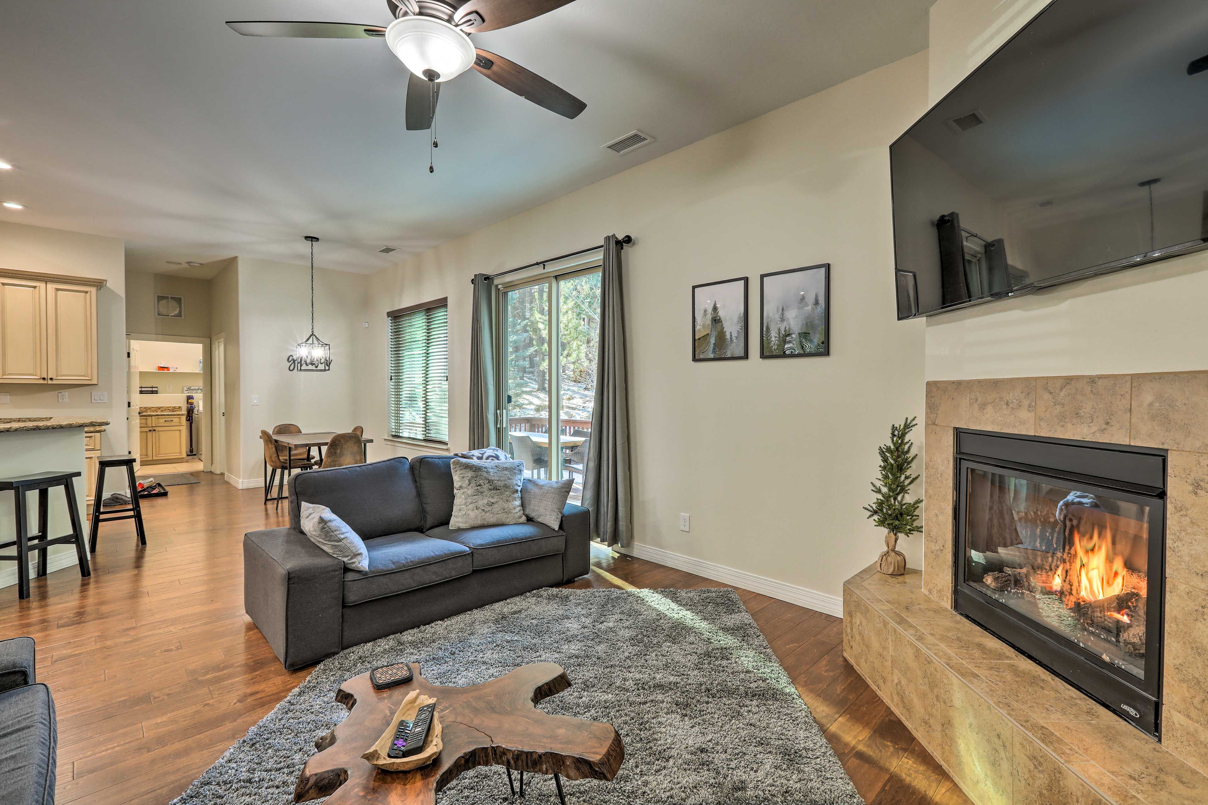 A modern living room with a fireplace, a ceiling fan, and a dining area in the background.