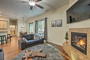 Ein modernes Wohnzimmer mit Kamin, Deckenventilator und Essbereich im Hintergrund.