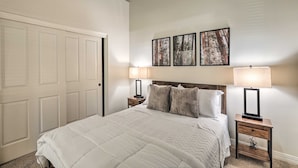 Une chambre à coucher avec un grand lit, deux tables de chevet avec des lampes, une tête de lit en bois et trois tableaux encadrés accrochés au mur.