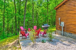 Eine Holzhütte mit Grillplatz und roten Stühlen in einer Waldlandschaft.