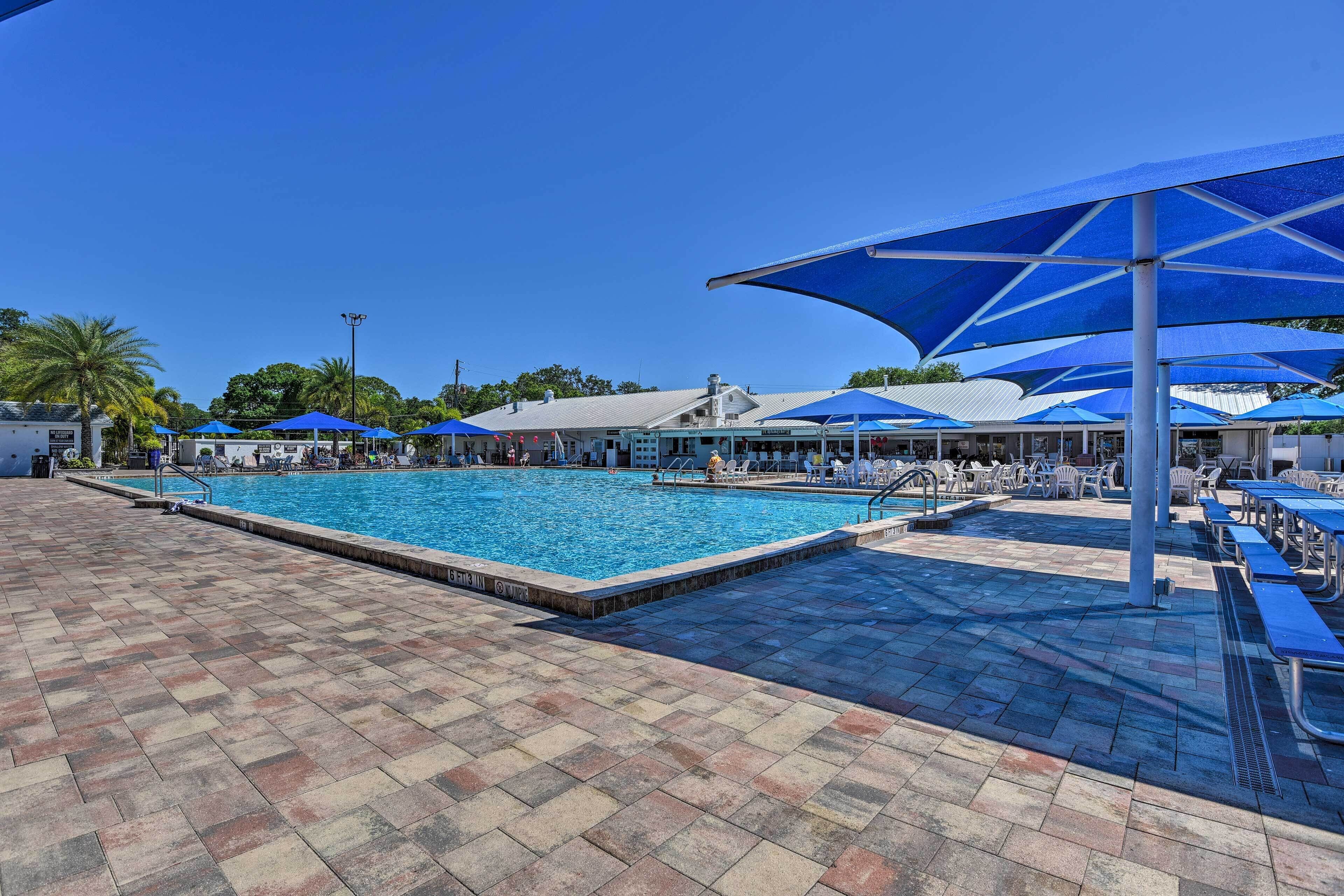 Une piscine bordée de parasols bleus, de chaises longues et d’une terrasse carrelée.
