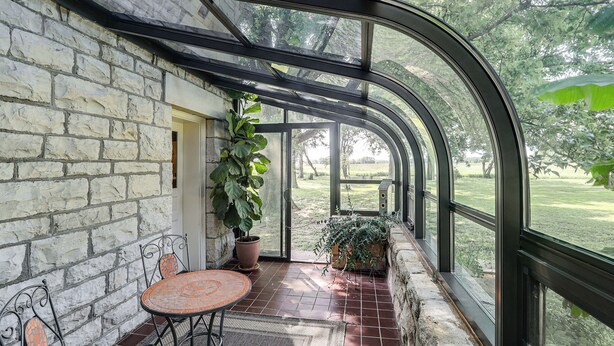 A covered patio with stone walls, a glass enclosure, a round table, and potted plants. - Pet-friendly Home: Grill & Fire Pit in Manhattan (Manhattan)
