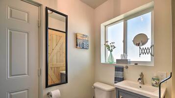 Un baño pequeño con inodoro, lavamanos y ventana con espejo.