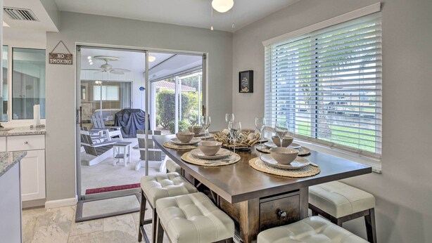 A modern dining area with a long table set for six, a ceiling fan, and a view of the backyard through glass doors. - Bright Home w/ Dock & Canal View in Cape Coral! (Cape Coral)