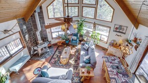 A spacious loft with a high ceiling, large windows, a stone fireplace, and a cozy seating area with a sofa and chairs. - Deck & Scenic Views: Munds Park A-frame Cabin (Munds Park)