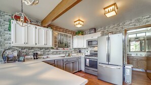 A kitchen with white cabinets, a stainless steel refrigerator, a microwave, and a stove. There is a brick wall and wooden beams on the ceiling. - Deck & Scenic Views: Munds Park A-frame Cabin (Munds Park)