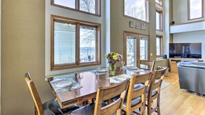 A dining area with a wooden table set for four, large windows, and a television in the background.