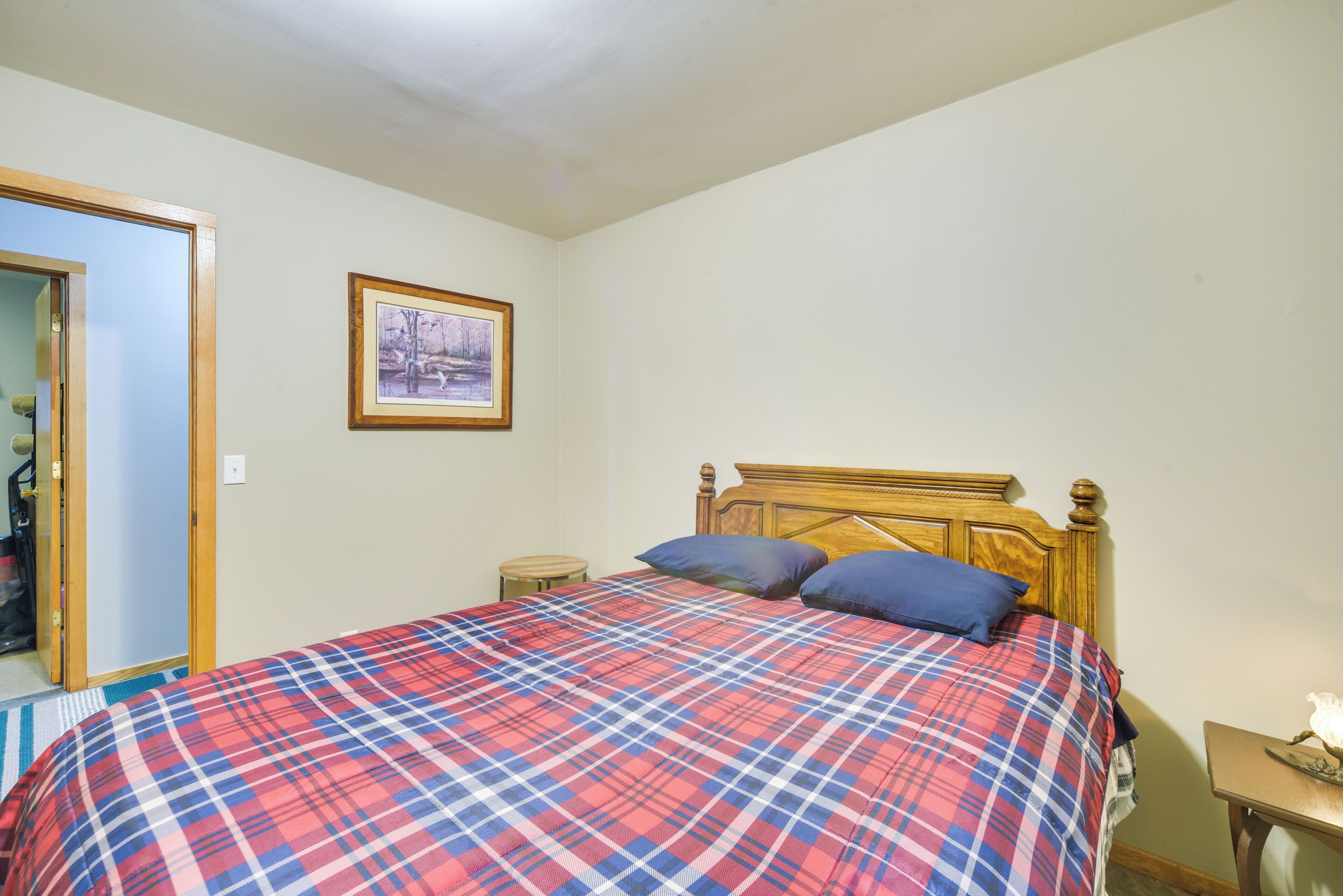Une chambre à coucher avec un lit en bois, une couverture à carreaux, un tableau encadré au mur et une petite table de chevet.