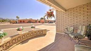 A covered patio with a brick wall, two striped chairs, and hanging flower baskets. - Patio & Mtn Views: 55 + Apache Junction Home! (Apache Junction)