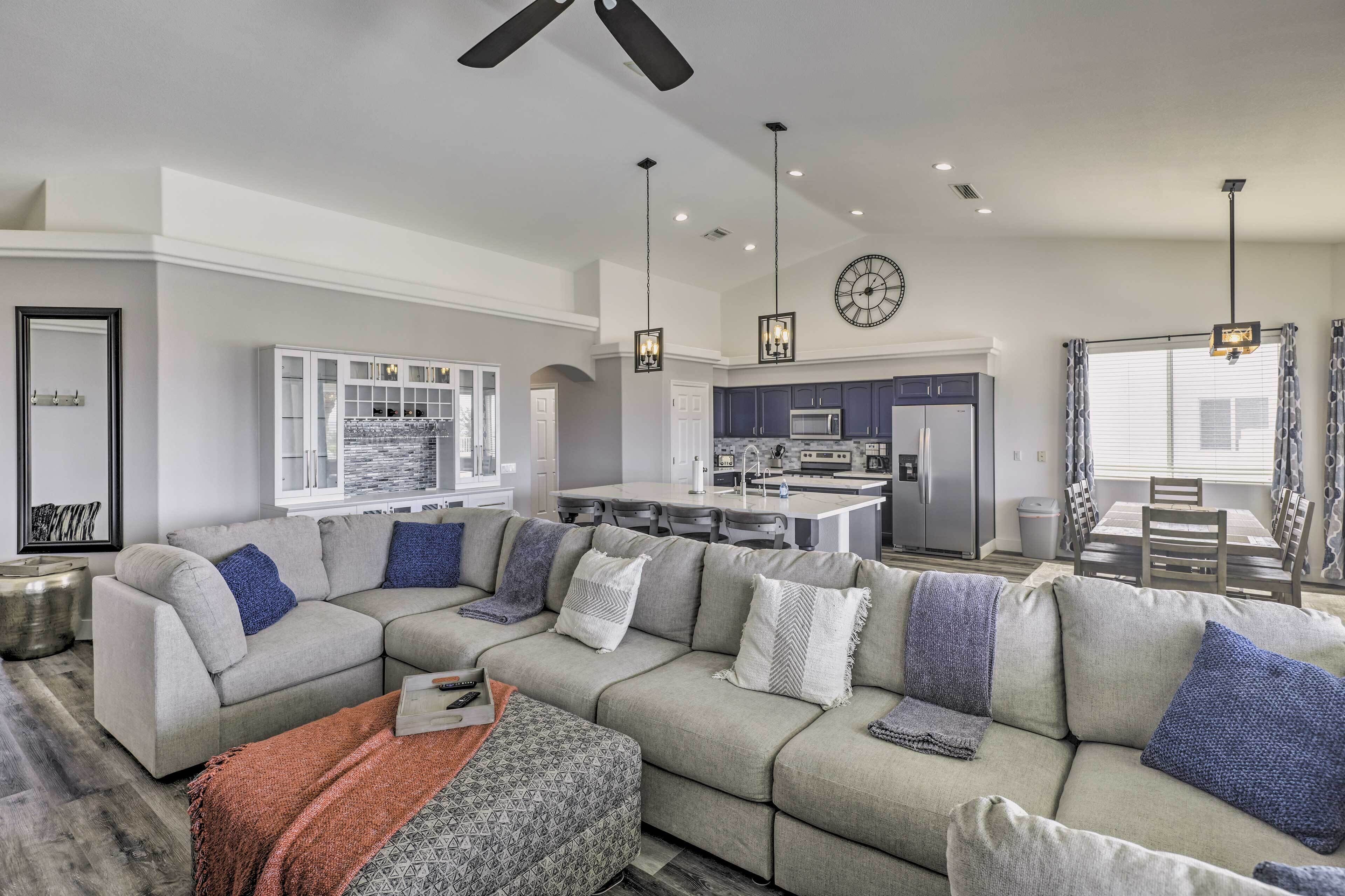 A modern living room with a sectional sofa, a dining area, and a kitchen with dark cabinets.