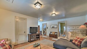 A living room with a sofa, a coffee table, a TV, and a cabinet. - Fire Pit & Beach: Lake Pleasant Home w/ Views (Speculator)