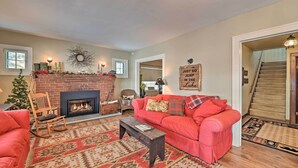 A cozy living room with a fireplace, a red sofa, a wooden rocking chair, and a Christmas tree. - Fire Pit & Beach: Lake Pleasant Home w/ Views (Speculator)