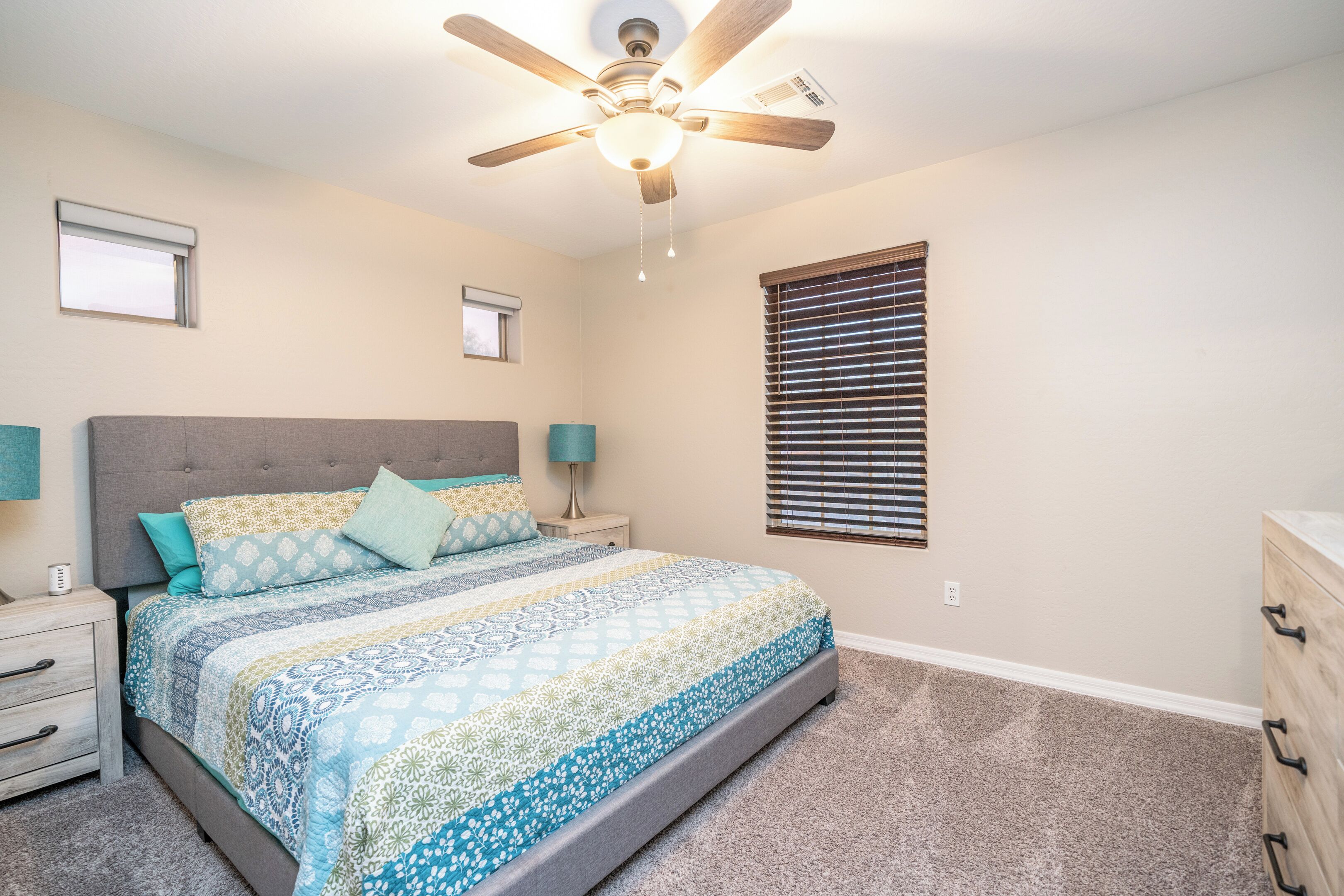 A bedroom with a bed, nightstands, a dresser, a ceiling fan, and a window with blinds.