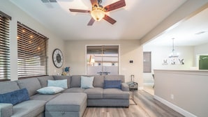 A living room with a sectional sofa, wooden flooring, a ceiling fan, and a view into the adjacent dining area. - Pool & Patio: Family-friendly Goodyear Home! (Goodyear)