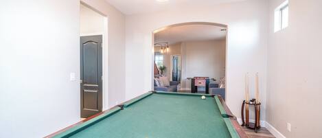 A pool table with balls, a billiard cue, and a pool table runner in a room with a wooden floor and white walls.