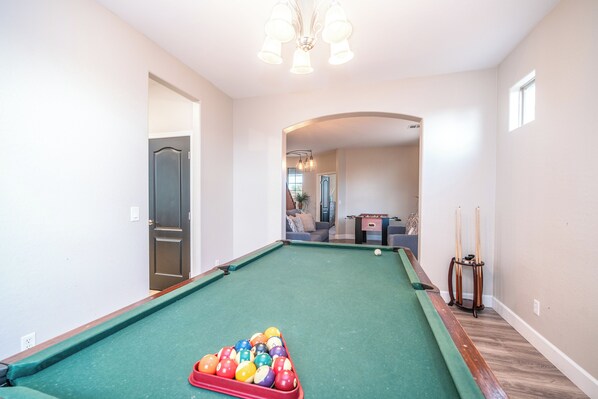 A pool table with balls, a billiard cue, and a pool table runner in a room with a wooden floor and white walls.