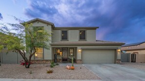 A two-story house with a front porch, a garage, and a landscaped front yard with a small tree and shrubs. - Pool & Patio: Family-friendly Goodyear Home! (Goodyear)