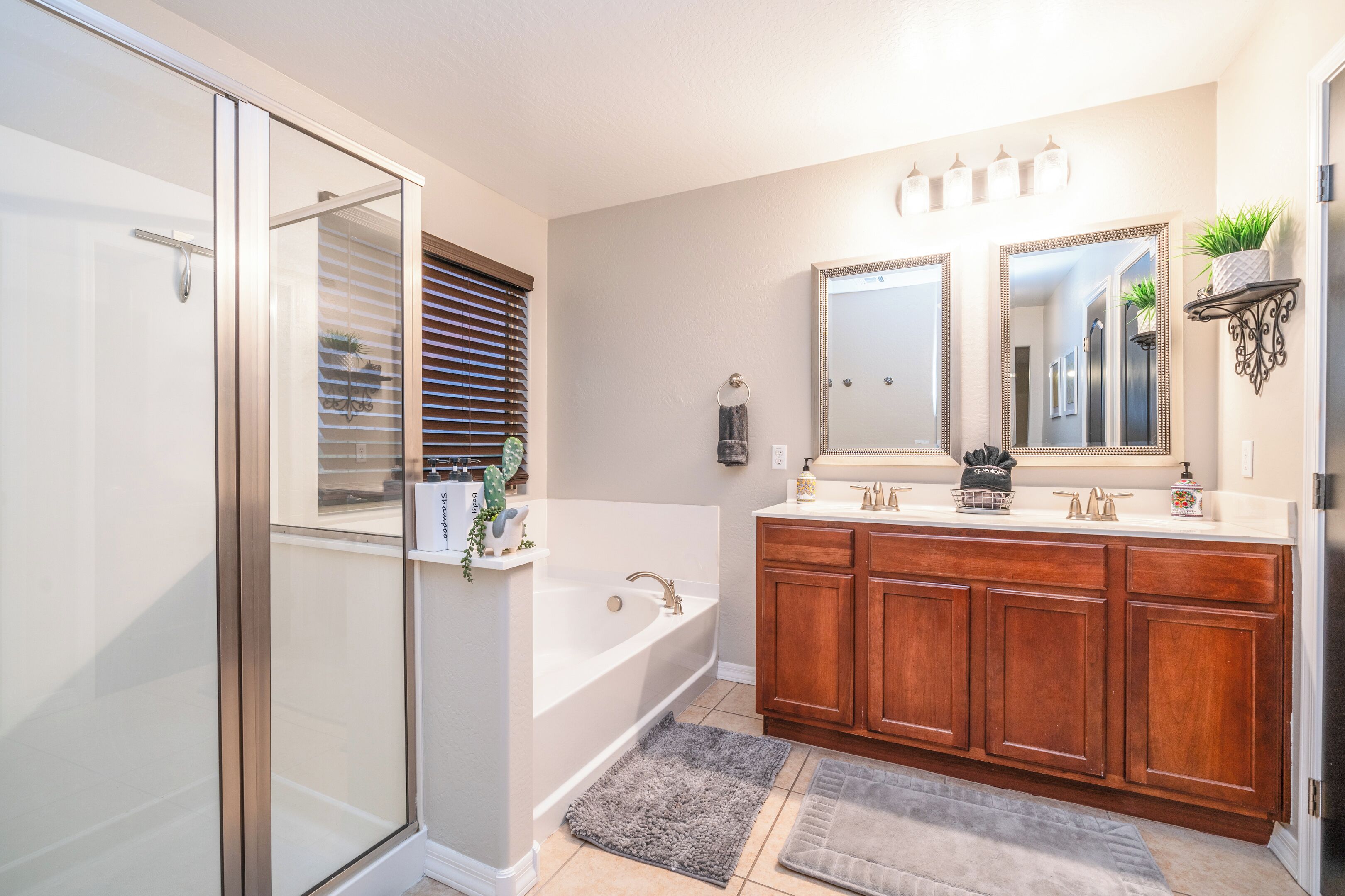 Un bagno moderno con box doccia in vetro, una vasca da bagno indipendente, mobili contenitori in legno e un grande specchio sopra il lavabo.