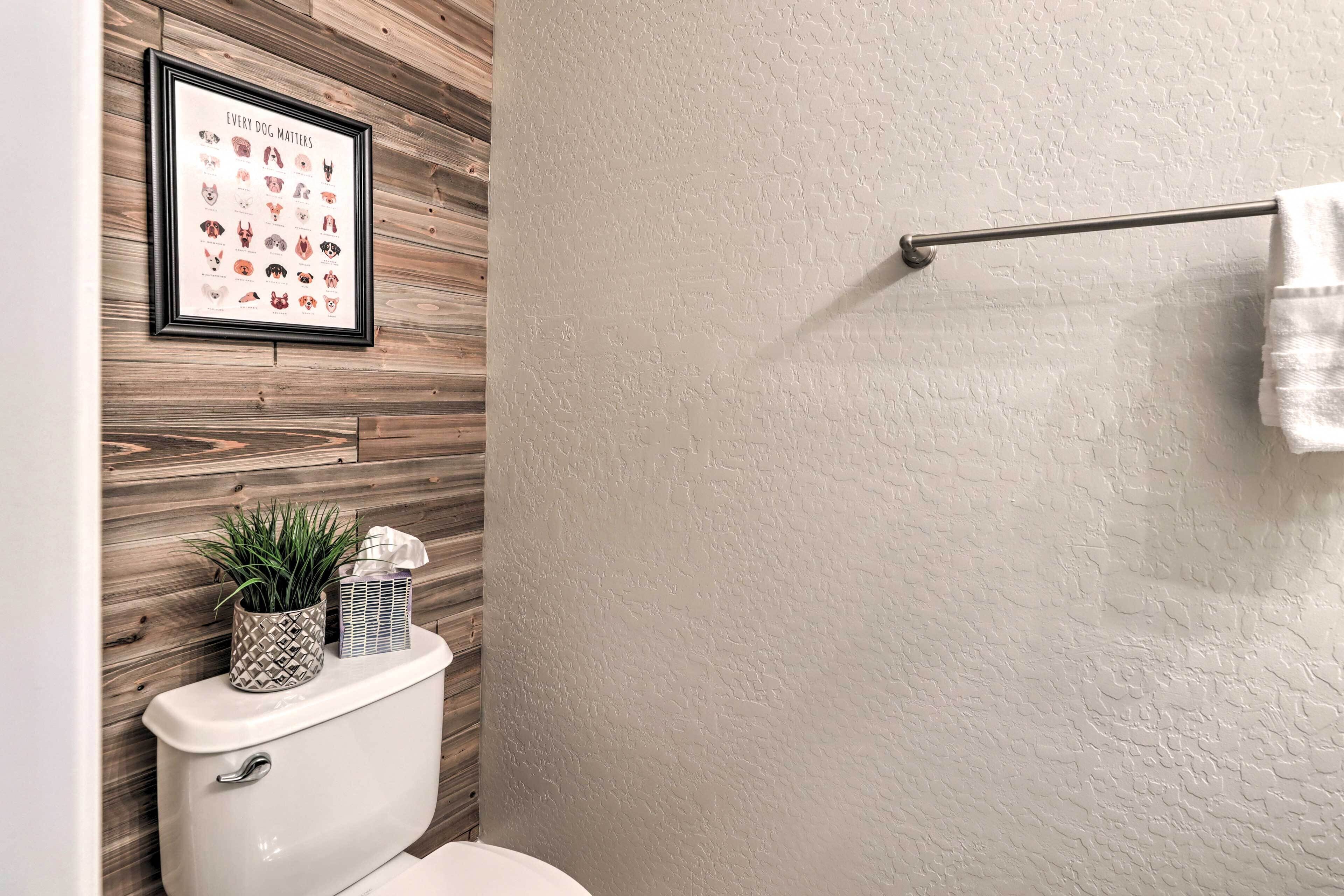 A bathroom with a wooden wall, a framed dog breed chart, a toilet, a towel rack, and a small potted plant.
