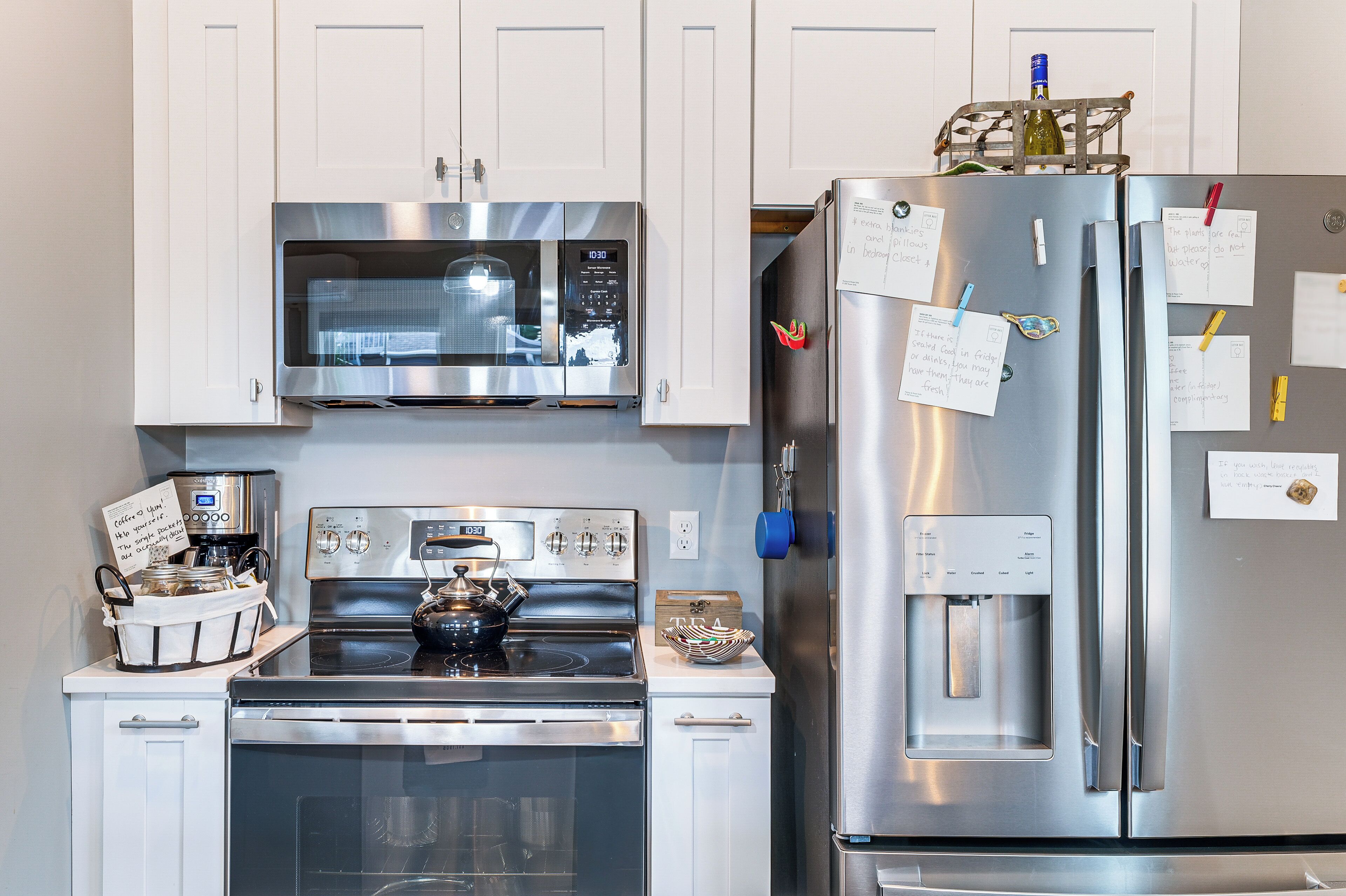 A modern kitchen with stainless steel appliances, including a microwave, oven, and refrigerator, with notes and magnets on the fridge.