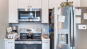 A modern kitchen with stainless steel appliances, including a microwave, oven, and refrigerator, with notes and magnets on the fridge.