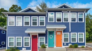A two-story blue house with a red and an orange door, surrounded by a brick pathway and small plants. - Walk to Dtwn: Charlevoix Condo w/ Fireplace (Charlevoix)