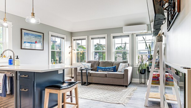 A modern kitchen with a central island, a grey sofa with a blue pillow, and a white ladder. - Walk to Dtwn: Charlevoix Condo w/ Fireplace (Charlevoix)