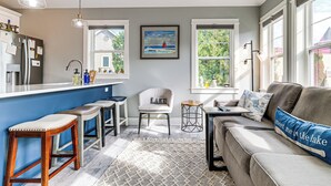 A modern kitchen with a bar area, a seating area with a sofa and chairs, and large windows providing natural light. - Walk to Dtwn: Charlevoix Condo w/ Fireplace (Charlevoix)
