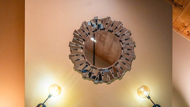 A stone fireplace with a wooden mantel, two wall-mounted lamps, and a decorative mirror above it. - Cozy Mountain Home at Rumbling Bald Resort! (Lake Lure)