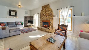 A living room with a stone fireplace, a grey sofa, a wooden coffee table, and a patterned rug. - 'dolorable' Home w/ Yard - Walk to River! (Dolores)