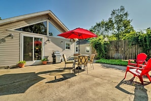 Une terrasse avec une table et des chaises, un parasol rouge et des plantes en pot.