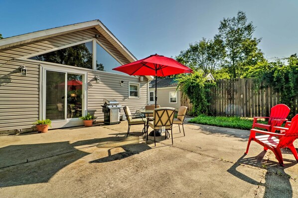 A patio with a table and chairs, a red umbrella, and potted plants.