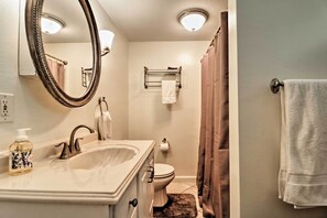 A bathroom with a sink, mirror, toilet, towel rack, and shower curtain.