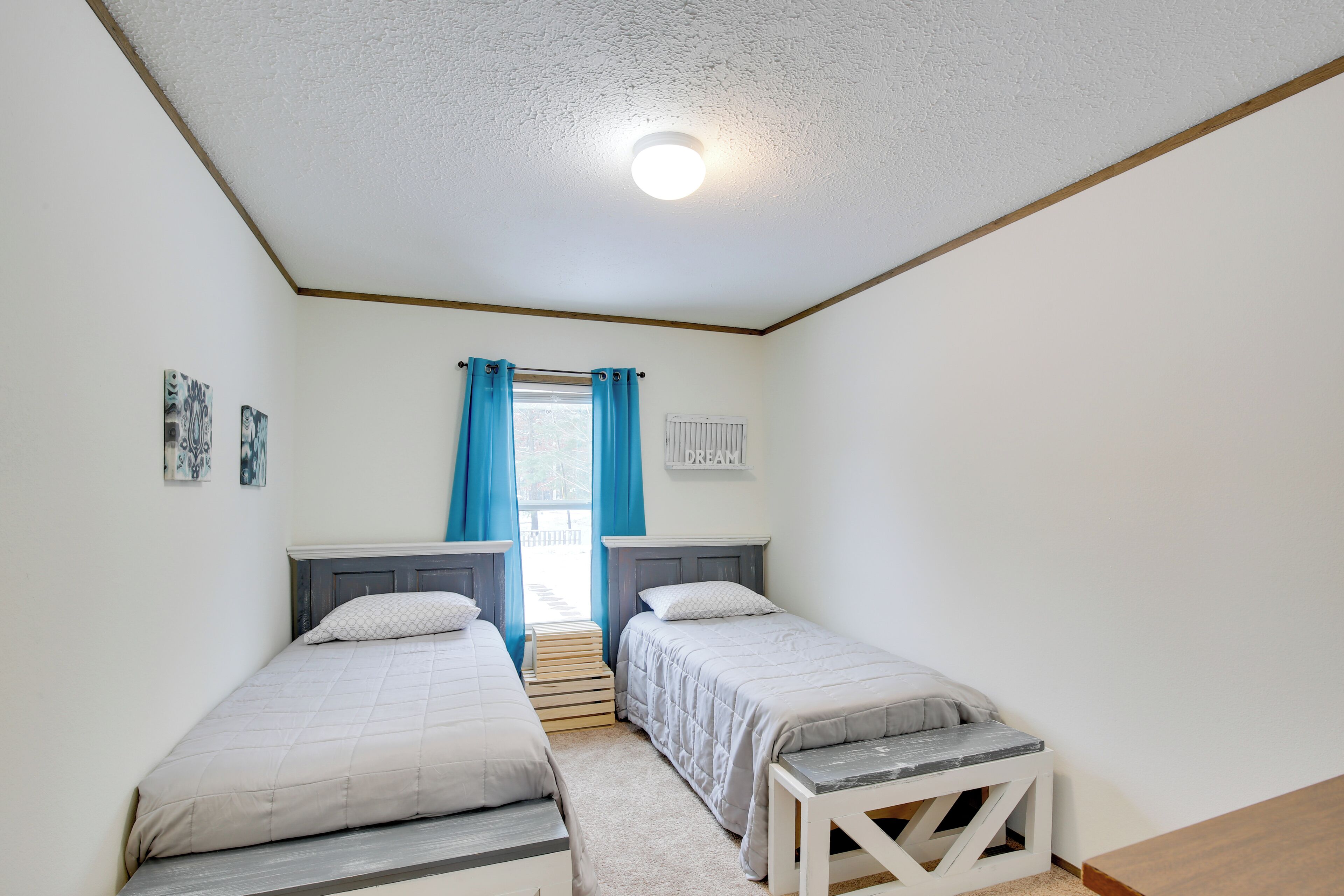 A bedroom with two single beds, a small table, a window with curtains, and a ceiling light.
