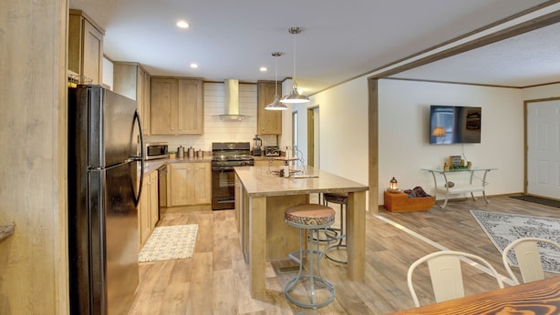 Une cuisine moderne avec des meubles en bois, un réfrigérateur noir, des appareils en acier inoxydable et un îlot central doté de tabourets de bar.