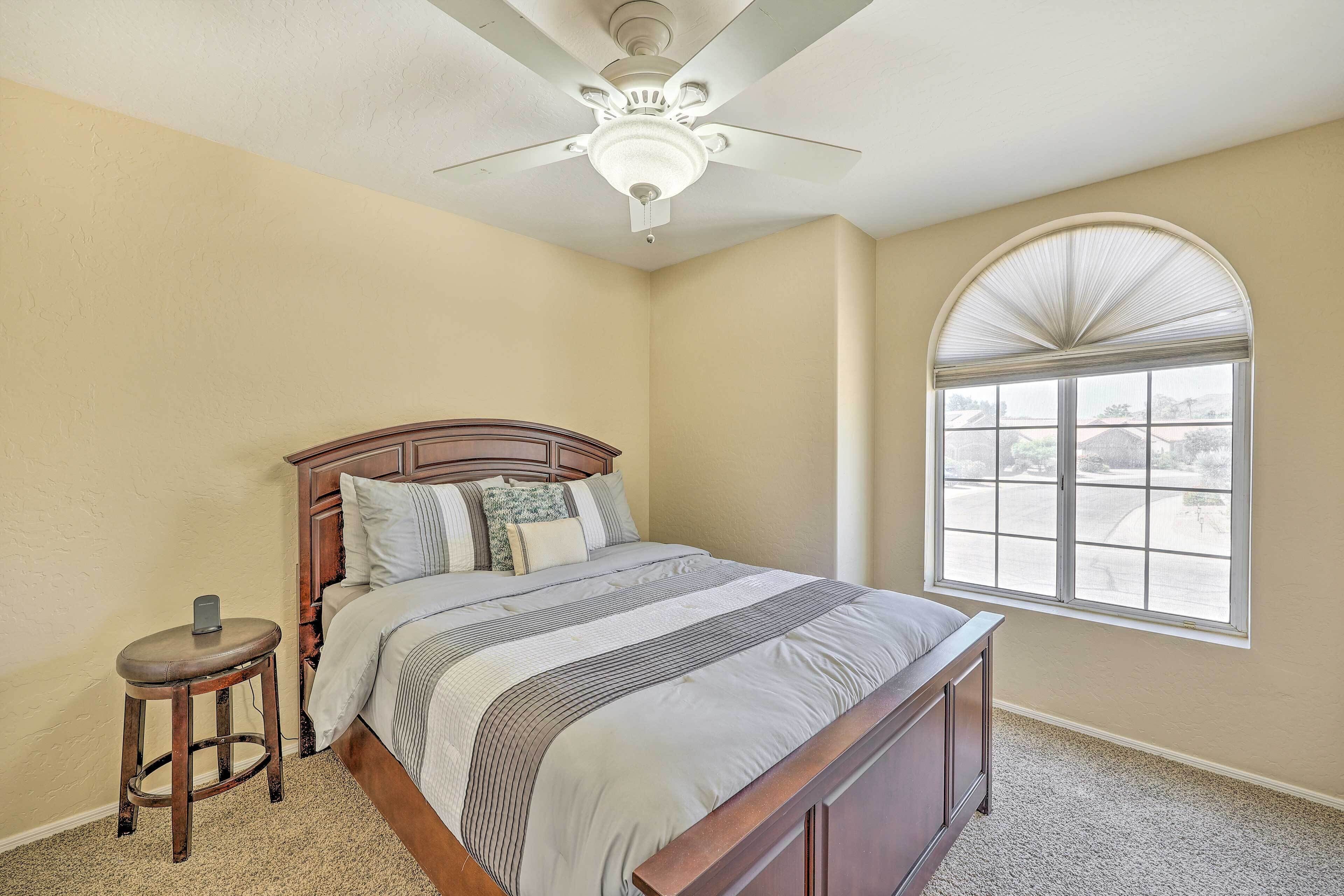 A bedroom with a bed, a nightstand, a ceiling fan, and a large window.