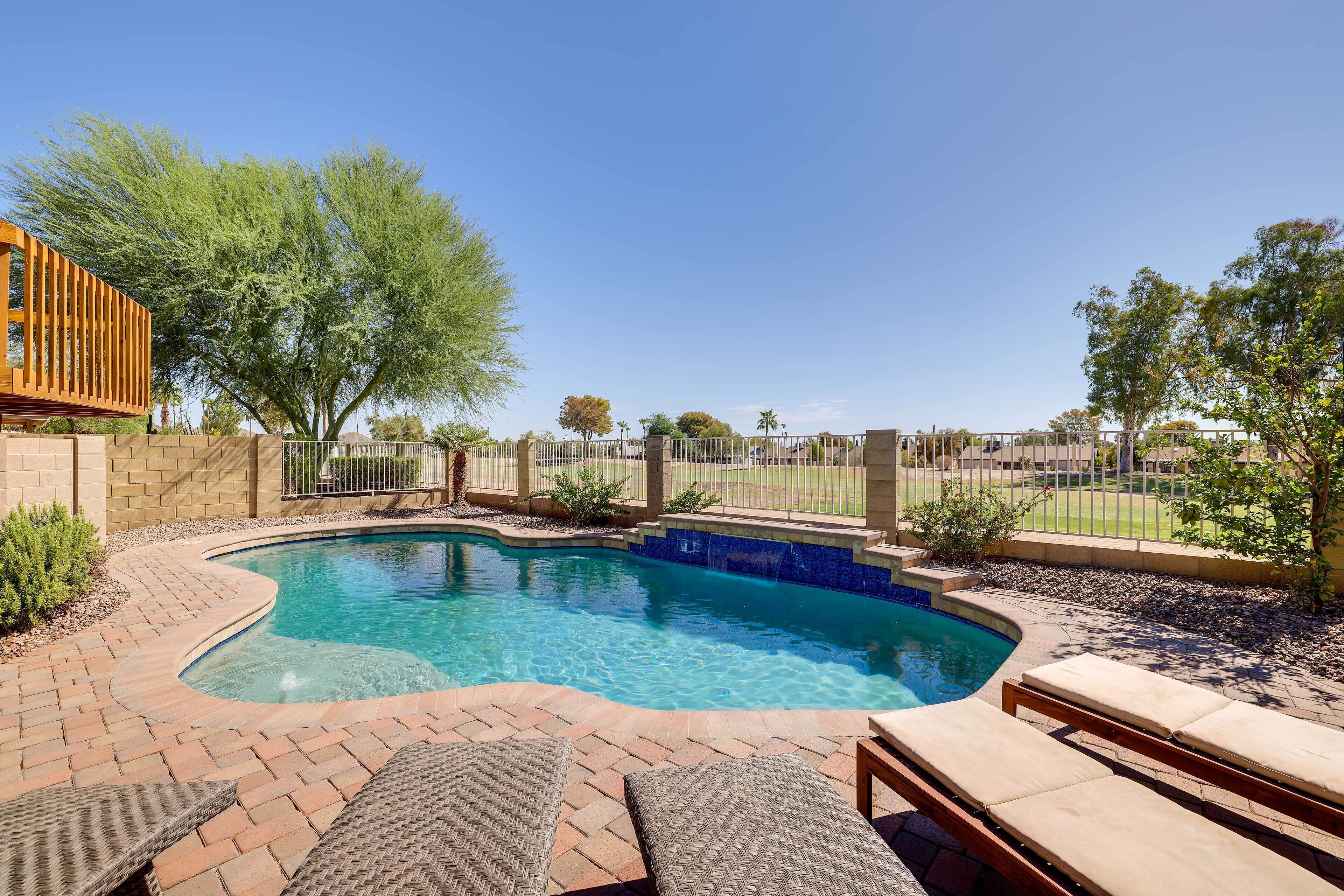 A swimming pool with a brick patio, lounge chairs, and a wooden deck.
