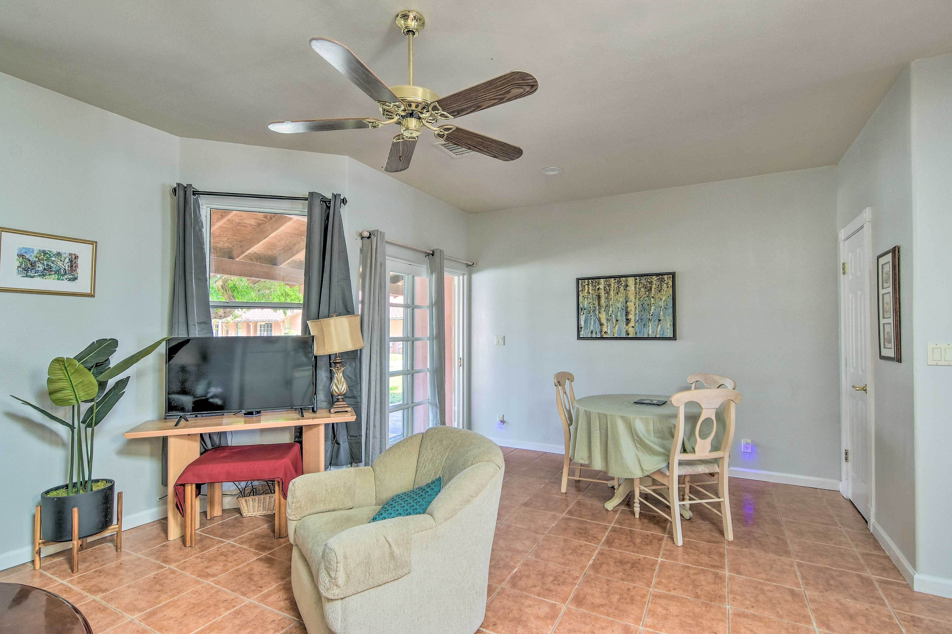 Un salon avec un téléviseur, un ventilateur de plafond, une table à manger avec des chaises et une plante en pot.