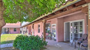Un patio couvert avec des chaises et une table, un petit jardin et un bâtiment à la façade rose et au toit en tuiles.