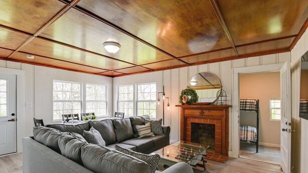 A spacious living room with a large gray sectional sofa, a glass coffee table, and a fireplace. There are multiple windows providing natural light, and a door leading to another room. - Chic Columbia Home < 2 Mi to Historic Square! (Columbia)