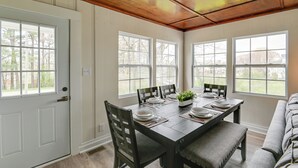A dining area with a wooden table set for four, surrounded by chairs, and large windows providing a view of the outdoors. - Chic Columbia Home < 2 Mi to Historic Square! (Columbia)