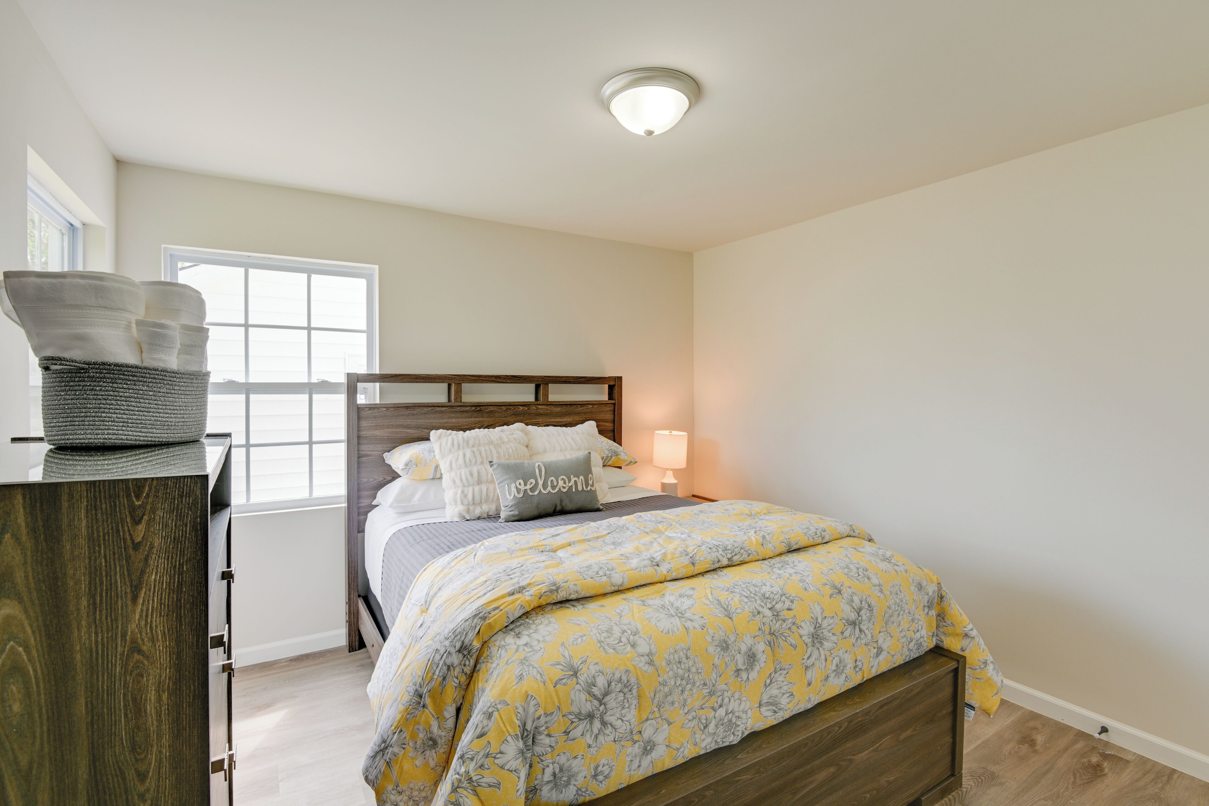 Une chambre à coucher avec une tête de lit en bois, un lit recouvert d’une couvre-lit à motifs floraux, une table de chevet avec une lampe et une fenêtre avec des stores.