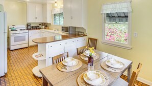 A compact kitchen with white cabinets, a stove, and a microwave. There's a dining table set with plates and a vase of flowers. - Central South Pasadena Apt, 3 Mi to Rose Bowl (South Pasadena)
