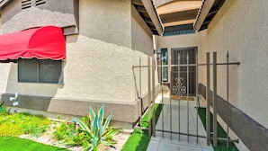 A residential building with a gated entrance, a red awning over a window, and a well-maintained garden with various plants. - Havasu Vacation Rental w/ Private Pool & Hot Tub! (Lake Havasu City)