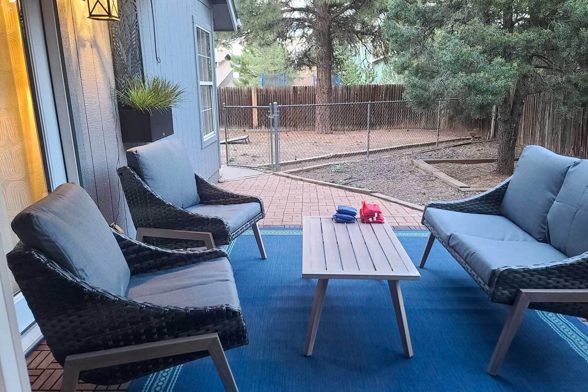 A patio with two wicker chairs and a small table, a blue carpet, and a wooden fence in the background.