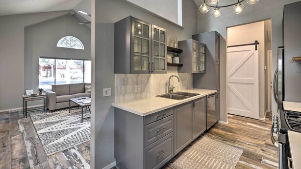 A modern kitchen with grey cabinetry, a white countertop, and a built-in oven. There is a window with a view of the outside, and a door leading to another room. - Modern Flagstaff Retreat ~ 4 Mi to Downtown! (Flagstaff)