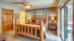 Een slaapkamer met een houten bed, een plafondventilator, een nachtkastje met een lamp en een groot raam.