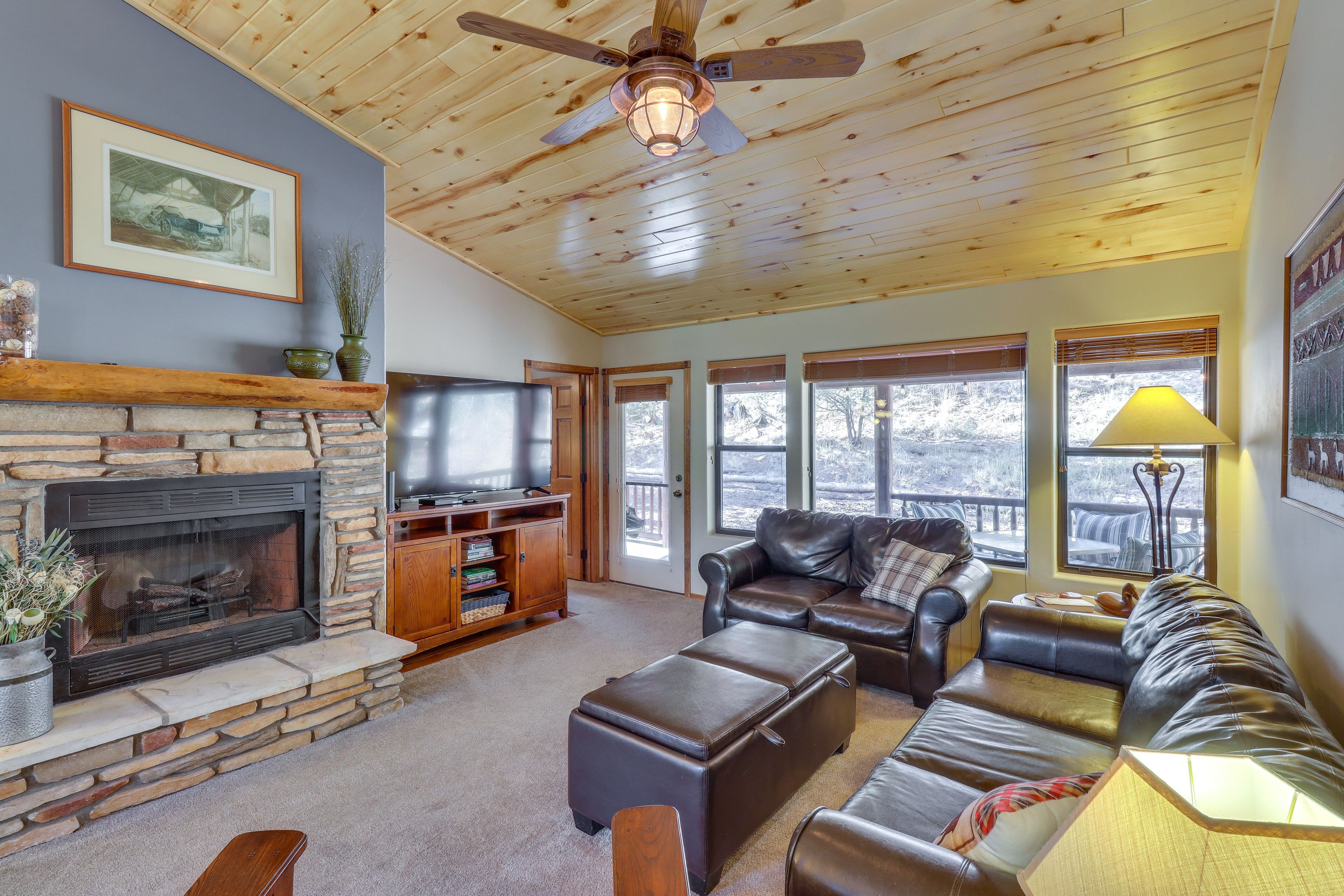 A cozy living room with a stone fireplace, leather sofas, a television, and large windows.